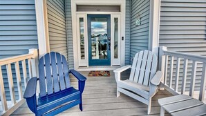Une véranda avec deux fauteuils Adirondack, une porte avec un panneau de verre et un petit tapis.