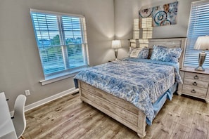 A bedroom with a bed, bedside tables, a window with blinds, and a wall-mounted artwork.