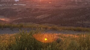 Un coucher de soleil sur une ville, avec des bâtiments bien visibles et un paysage vallonné.