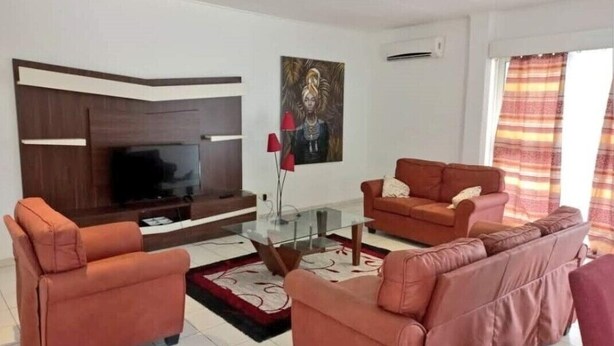 A living room with a flat-screen TV, two sofas, a glass coffee table, and a painting on the wall. - Magnifique Appartement Meublé Avec Piscine à Pointe Noire (Pointe-Noire)