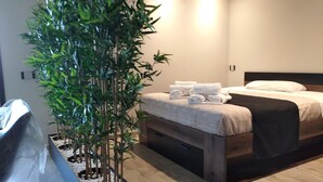 Une chambre d’hôtel moderne avec un lit, une grande plante en pot et un plancher en bois.