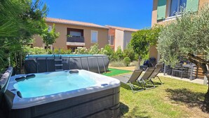 Un jacuzzi et des chaises longues dans un jardin, avec un bâtiment visible à l’arrière-plan.