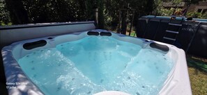 A hot tub with a clear blue water surface, surrounded by a wooden deck and a metal fence.