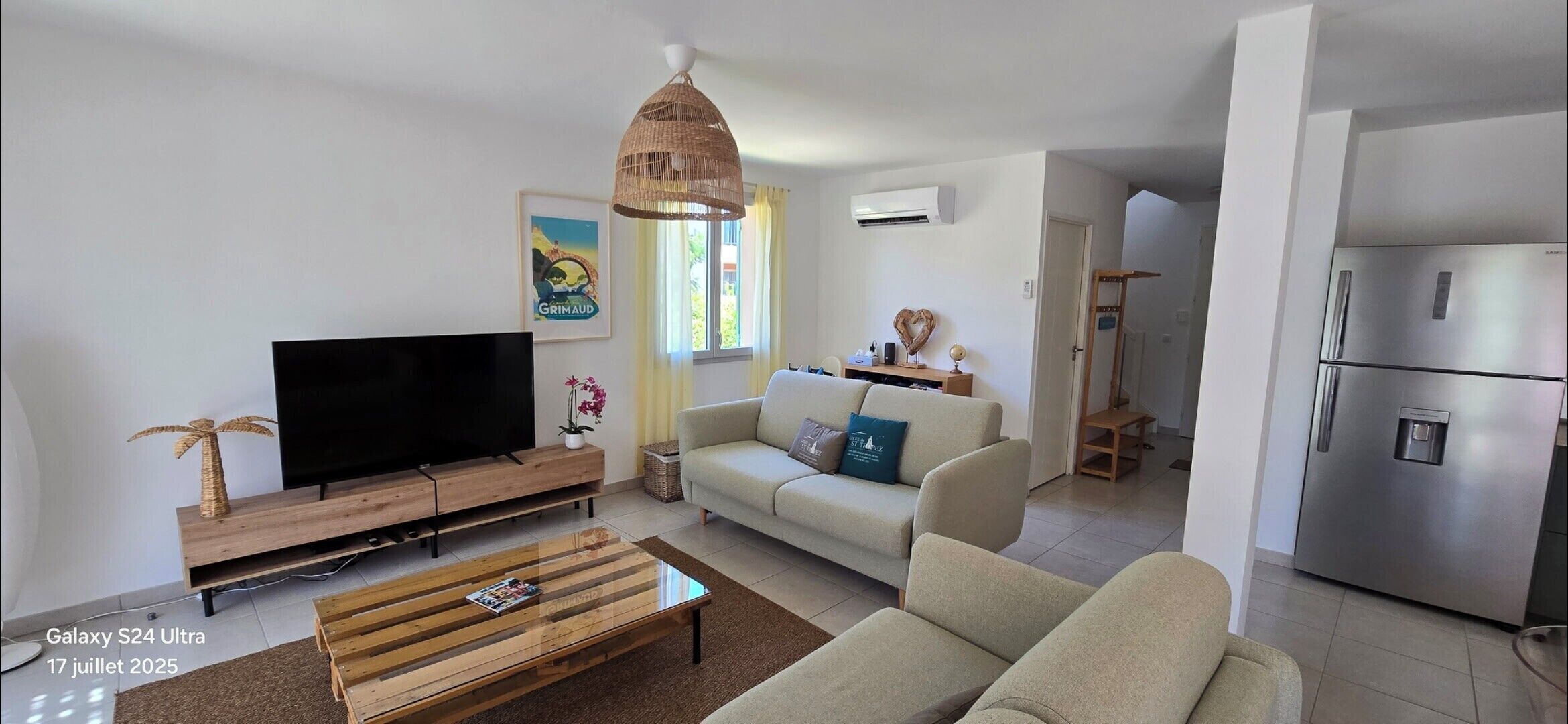 A modern living room with a flat-screen TV, wooden coffee table, sofa, and a dining area with a table and chairs.