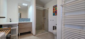 A modern bathroom with a glass shower enclosure, a white toilet, and a colorful artwork on the wall.