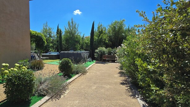 Un jardin avec un chemin de gravier, des plantes vertes et un jacuzzi.