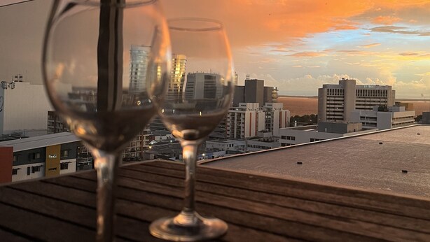 Two empty wine glasses on a wooden surface with a cityscape view in the background. - Darwin City Hotel Suite with Sea View & Balcony  (Darwin City)