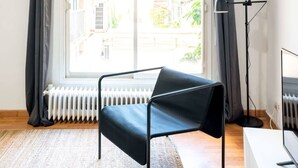 Ein Zimmer mit einem Bett, einer Stehlampe, einem Heizkörper und Blick auf Gebäude durch ein blickdichtes Fenster.