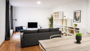 Ein modernes Wohnzimmer mit einer Couch, einem Fernseher, einem Esstisch und einem Bücherregal.