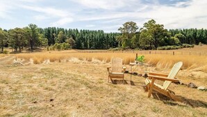 Ein Feld mit zwei Holzstühlen und einem Tisch, umgeben von trockenem Gras und Bäumen.