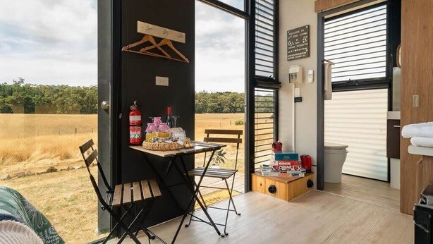 Ein modernes Zimmer mit großem Fenster, Tisch mit Snacks, Stuhl und kleiner Holzkommode.