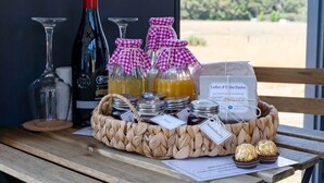 Ein Korbkörbchen mit Gläsern voll Marmelade, einer Weinflasche und einem Glas auf einem Holztisch.