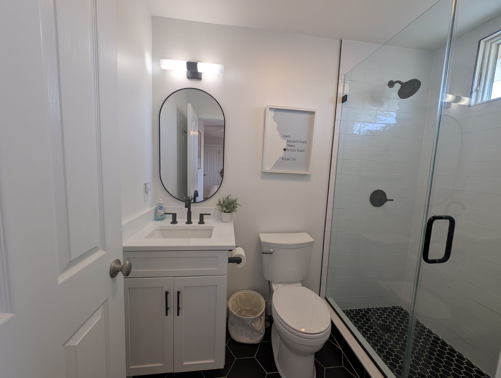 A modern bathroom with a white sink, mirror, toilet, and glass-enclosed shower.