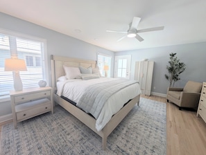 A bedroom with a bed, nightstands, a ceiling fan, a wardrobe, and a plant.