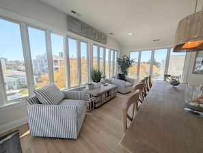 A sunlit room with large windows, a striped sofa, a wooden dining table, and a sign reading 'BEACH'.
