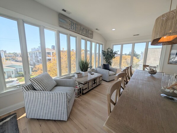 A sunlit room with large windows, a striped sofa, a wooden dining table, and a sign reading 'BEACH'.
