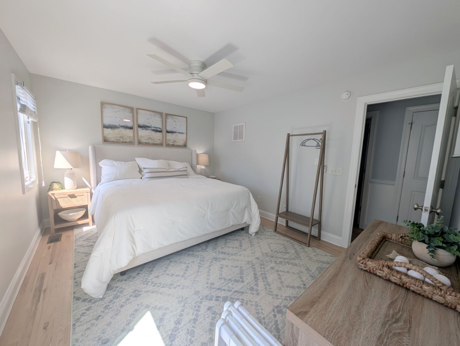 Un dormitorio con cama, mesitas de noche, ventilador de techo, espejo, cómoda de madera y una puerta.