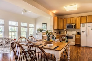 A kitchen with wooden cabinets, a microwave, a stove, and a dining area with a table and chairs. - 4 bedroom Dog Friendly home with community pool (Ocean View)