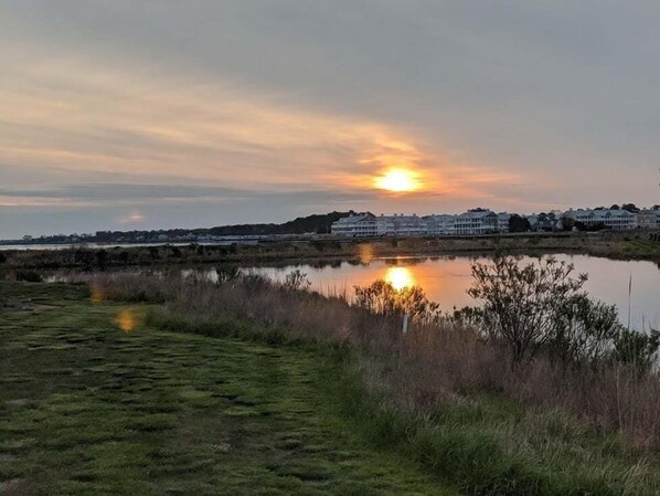 A sunset over a body of water with a row of houses in the background. - Waterview 1st floor 2 bedroom condo with pool access (Ocean View)
