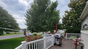 A wooden deck with a white railing, outdoor furniture, and a grill.