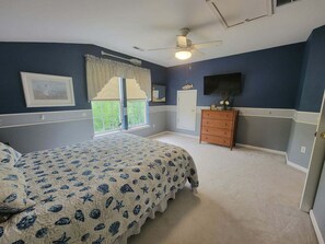 Une chambre à coucher avec un lit, une commode, une fenêtre et un ventilateur de plafond.