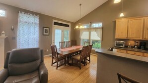 A dining area with a wooden table and chairs, a kitchen with wooden cabinets, and a window with curtains.