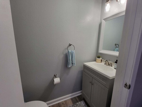 A bathroom with a grey wall, a white sink, a mirror, a towel, and a toilet paper holder.