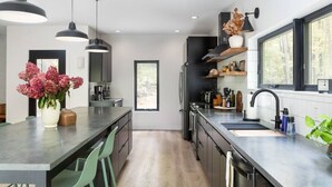 Una cocina moderna con una isla central, iluminación colgante y vistas al exterior a través de amplios ventanales.
