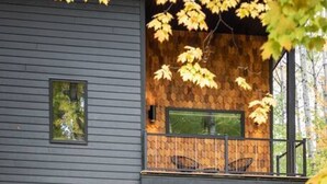 Una casa moderna de dos pisos con balcón, ventanas amplias y una zona de terraza de madera.