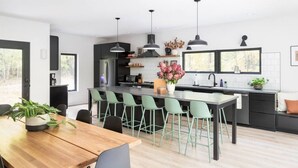 Una cocina moderna con una isla central, taburetes de bar, iluminación colgante y vistas al exterior.