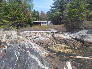 A cabin with a wooden deck, surrounded by rocky terrain and dense forest.