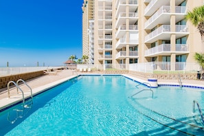 A swimming pool with a clear blue water, surrounded by a white fence, and a tall building with balconies in the background.