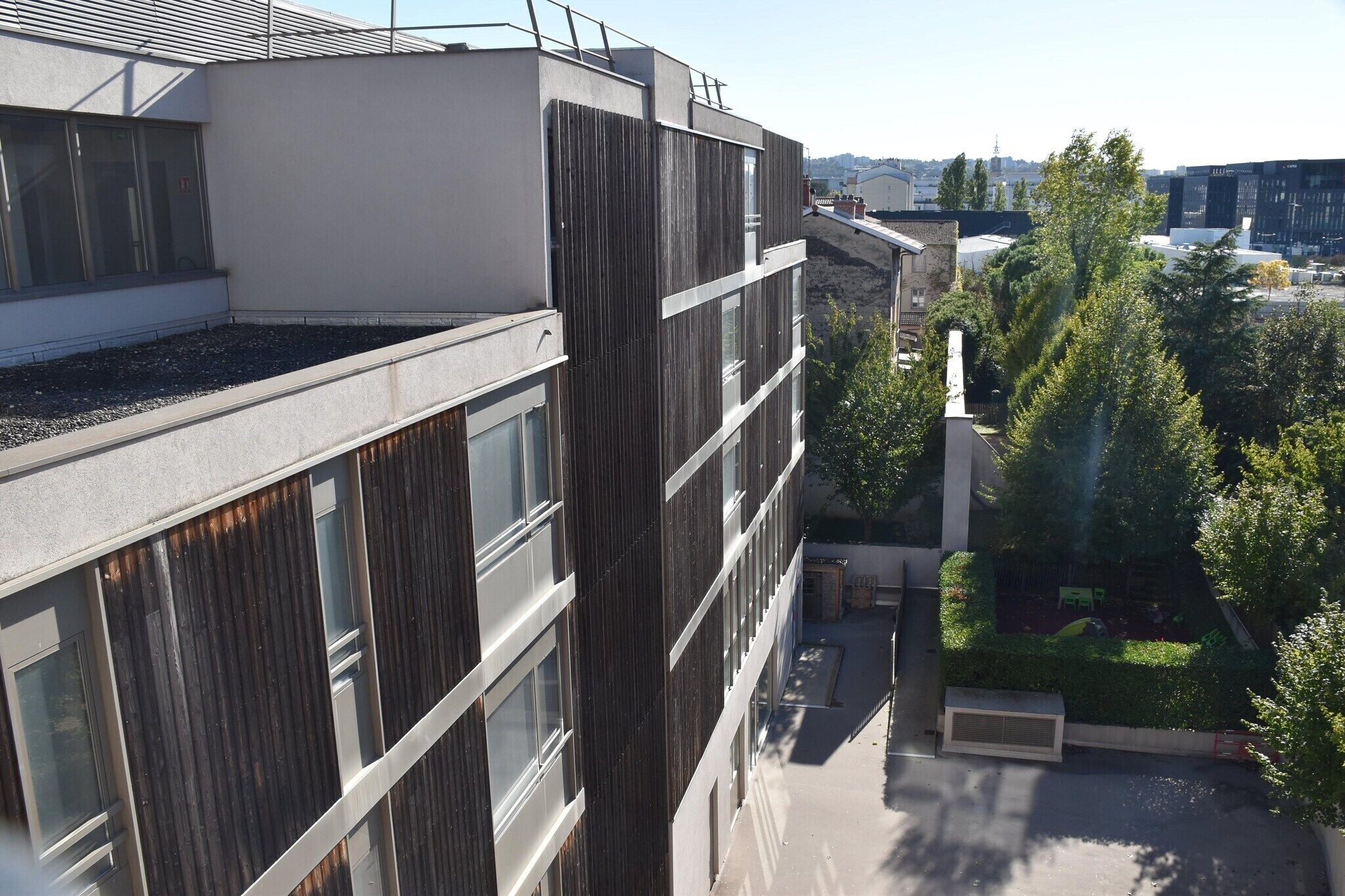 A modern building with a rooftop terrace, large windows, and a small garden area.