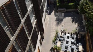Eine Vogelperspektive zeigt einen Innenhof mit Außenbestuhlung und ein Gebäude mit großen Fenstern.
