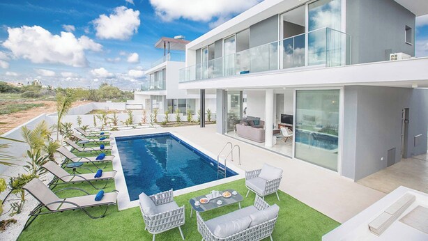 A modern two-story house with a swimming pool, outdoor furniture, and a view of the landscape.