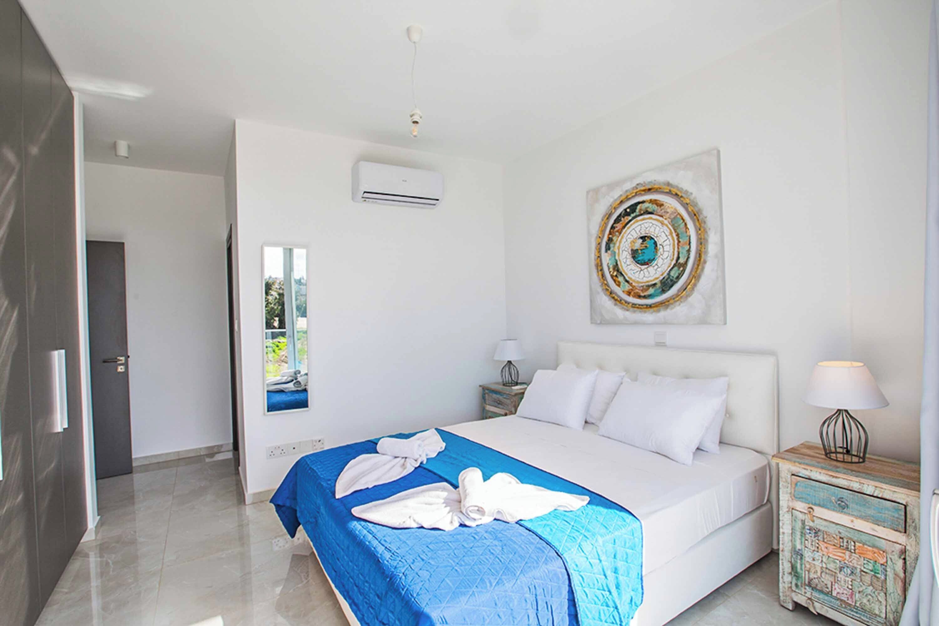 A modern hotel room with a large bed, a blue and white bedspread, a decorative wall piece, and a small bedside table with a lamp.