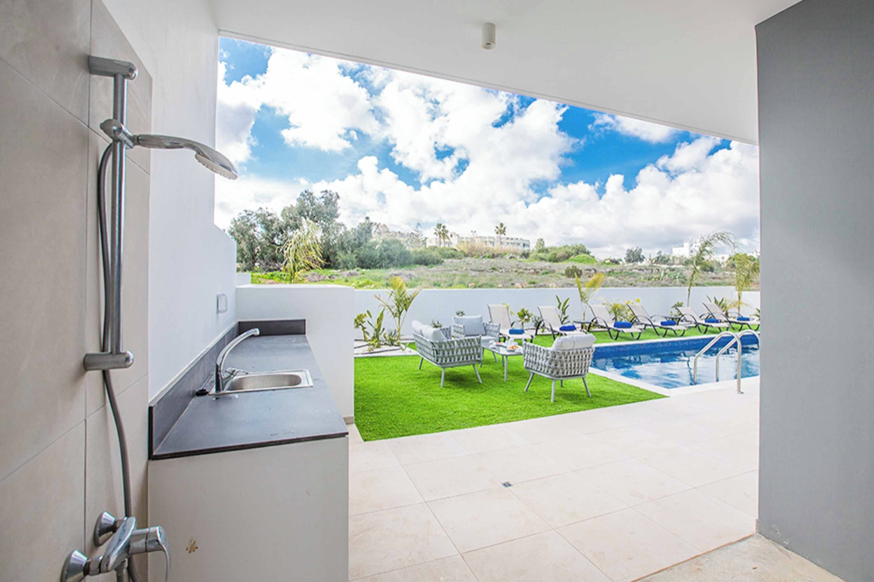 Casa de banho moderna com chuveiro, pia e vista para a piscina e área de estar exterior.