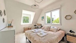 A bedroom with a large bed, a desk, a chair, a dresser, and a window.