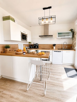 A modern kitchen with white cabinets, a wooden countertop, a stainless steel sink, and a bar stool.