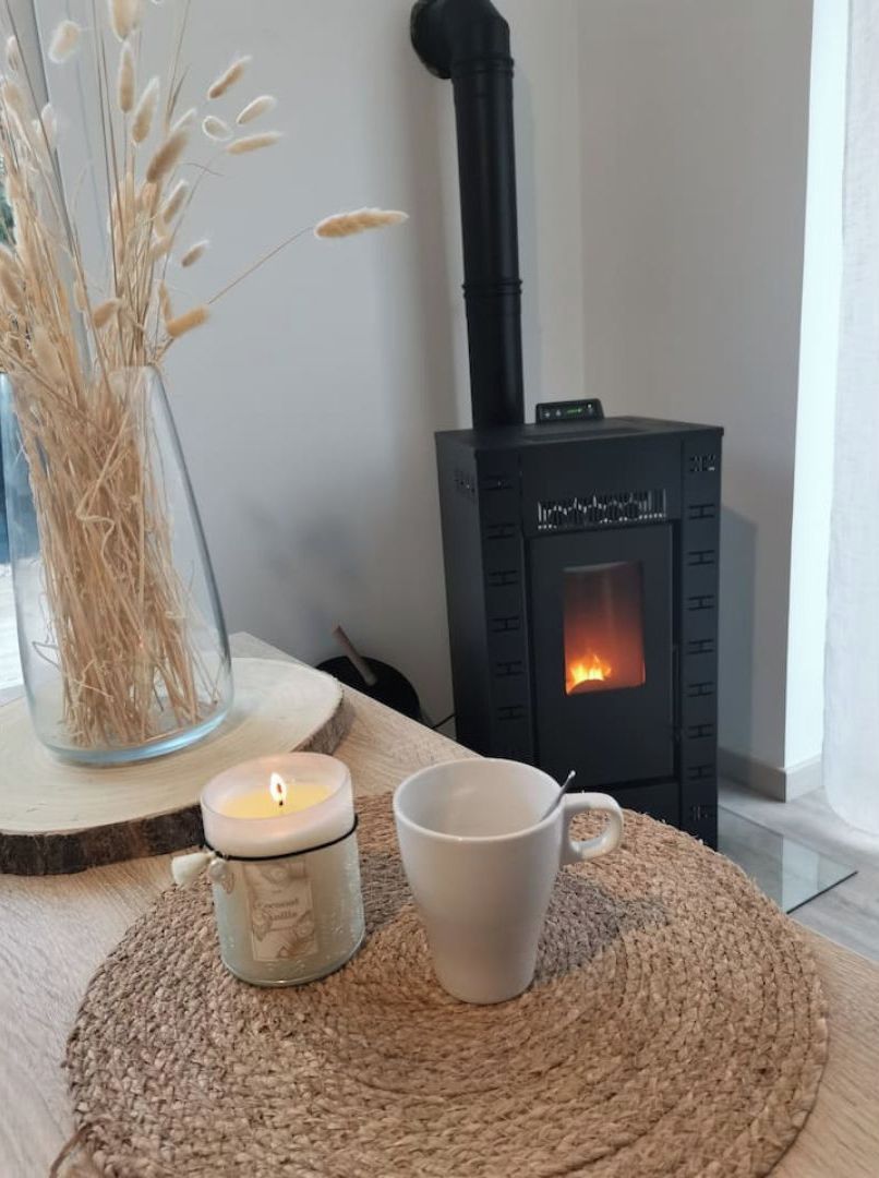 Une pièce chaleureuse avec un poêle à bois, une bougie et une tasse posée sur un tapis en fibres naturelles.