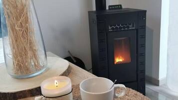 Une pièce chaleureuse avec un poêle à bois, une bougie et une tasse posée sur un tapis en fibres naturelles.