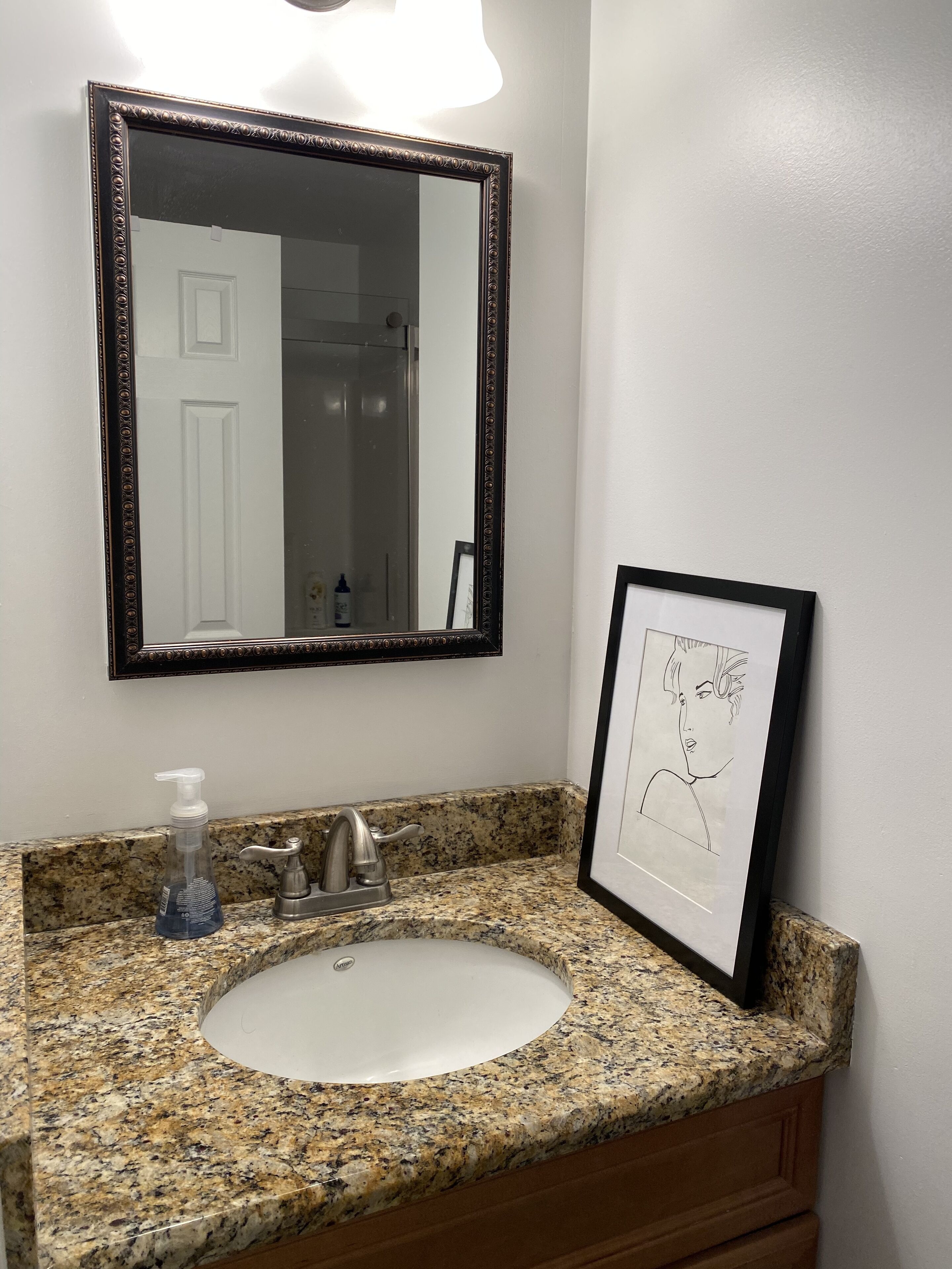 A bathroom with a granite countertop, a white sink, a framed picture, and a mirror with a dark frame.