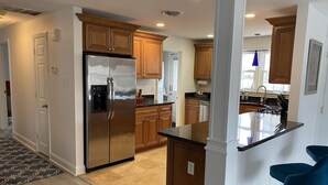 A modern kitchen with wooden cabinets, a stainless steel refrigerator, and a bar area with blue chairs. - Ventnor newly renovated beach condo (Ventnor City)