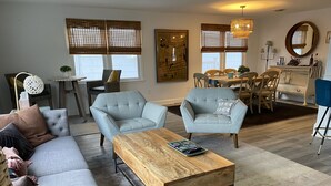 A modern living room with a grey sofa, two armchairs, a wooden coffee table, and a dining area with a table and chairs. - Ventnor newly renovated beach condo (Ventnor City)