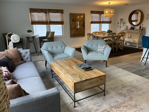 Un salon moderne avec un canapé gris, deux fauteuils, une table basse en bois et un coin repas comprenant une table et des chaises.