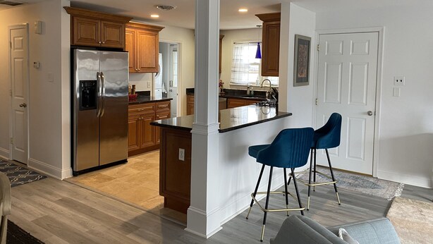 A modern kitchen with wooden cabinets, a stainless steel refrigerator, and a bar area with two blue bar stools. - Ventnor newly renovated beach condo (Ventnor City)