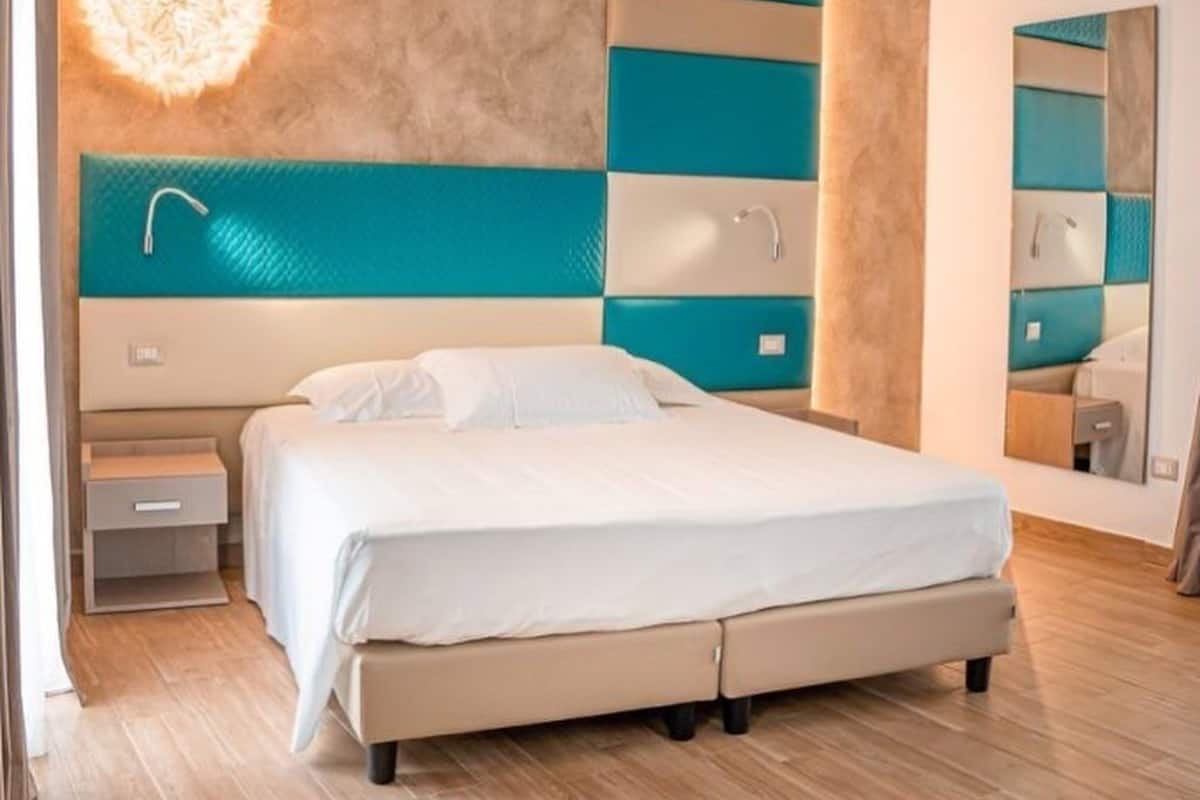 Un dormitorio moderno con una cama grande, una mesita de noche, una lámpara de pared y un espejo.