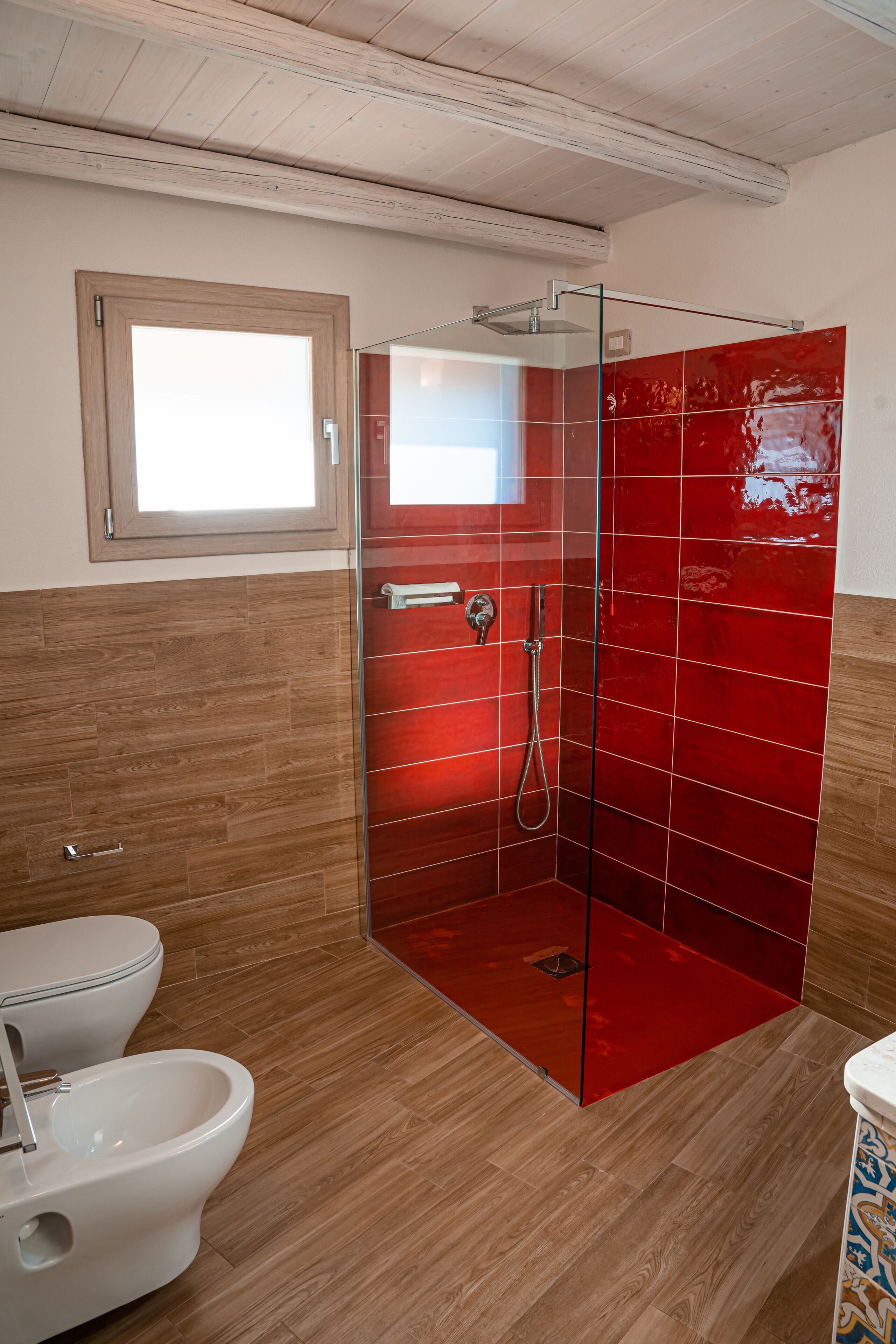 A bathroom with a glass-enclosed shower, wooden flooring, a white toilet, and a bidet.