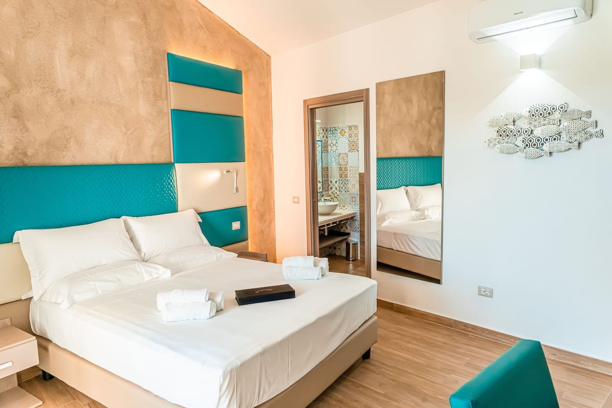 Una habitación de hotel moderna con una cama grande, una mesita de noche, un espejo y un aire acondicionado de pared.
