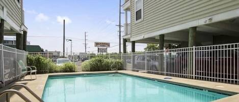 A swimming pool with a metal fence, surrounded by buildings.